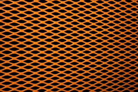 Gold colored metal grill of diamond shaped mesh, against black.の写真素材