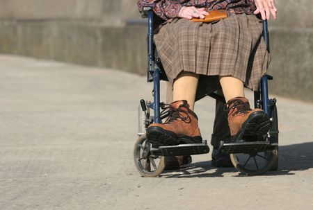 Lower body of a an elderly woman sitting in a wheelchair on a pavement, with arthritic hands and wearing large boots. の写真素材