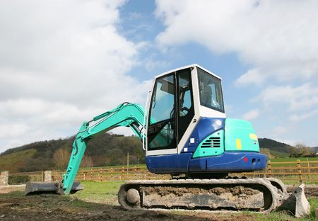 Mini digger standing idle on rough ground in rural countryside. 