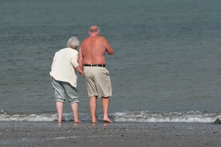 Elderly retired female and male holding hands and paddling together in the sea.の写真素材