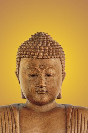 Wooden Buddha with eyes closed in prayer over a glowing golden background.の写真素材