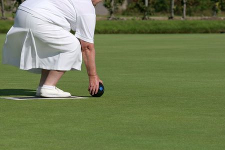 Lower body of an elderly female wearing white clothing and holding a lawn bowling ball about to bowl. の写真素材