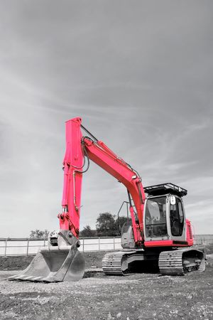 Industrial pink digger with excavator bucket standing idle on a building site. Desaturated with only the metal on the vehicle saturated.の写真素材