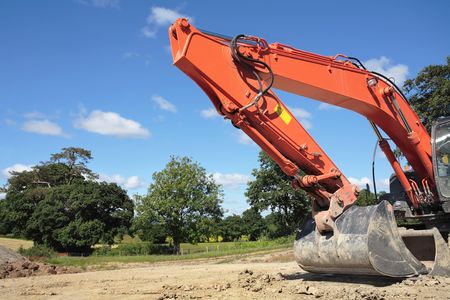 Industrial orange digger bucket with hydraulics standing idle in rural countryside, against a blue sky and clouds.の写真素材