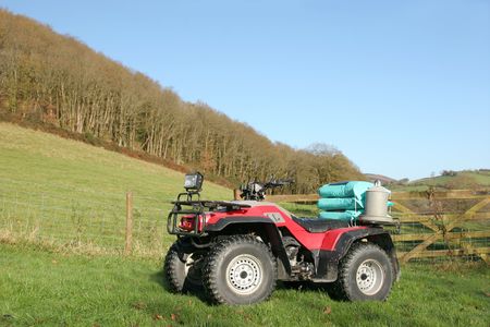 Quad bike standing in a field in rural countryside and set against a blue sky.