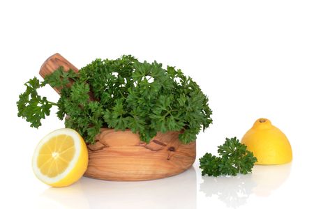 Parsley herb leaf sprigs in an olive wood mortar with pestle and two lemon halves, over white background.の写真素材