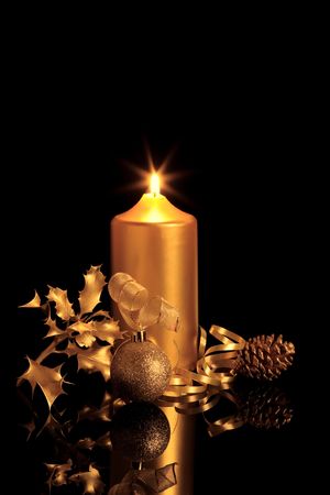  Golden christmas decorations in candlelight including sparkling bauble, ribbon, holly and pine cone, over black background with reflection.の写真素材