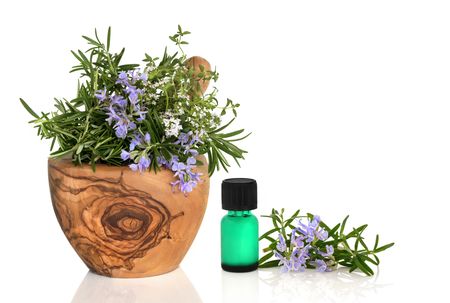  Rosemary and thyme herbs in flower in an olive wood mortar with pestle with an aromatherapy oil glass bottle and leaf sprig isolated over white background.の写真素材