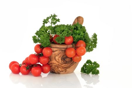 Tomatoes on the vine and parsley herb leaf sprigs in an olive wood mortar with pestle, over white background.の写真素材