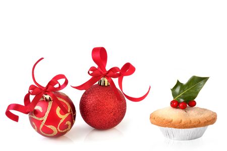 Christmas baubles in sparkling red and gold with ribbons and mince pie with a holly sprig and berries, over white background with reflection.の写真素材