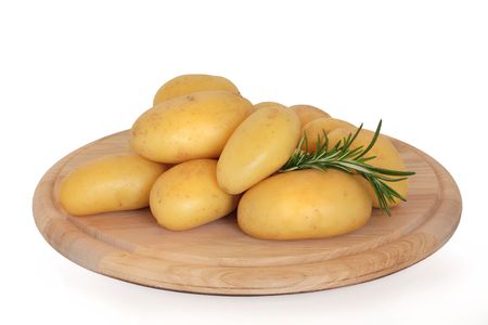 New potatoes with a rosemary herb leaf sprig on a circular wooden board, over white background.の写真素材