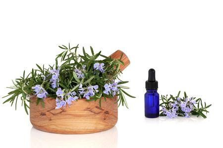 Rosemary herb with flowers in an olive wood mortar with pestle and aromatherapy essential oil dropper glass bottle, over white background.の写真素材