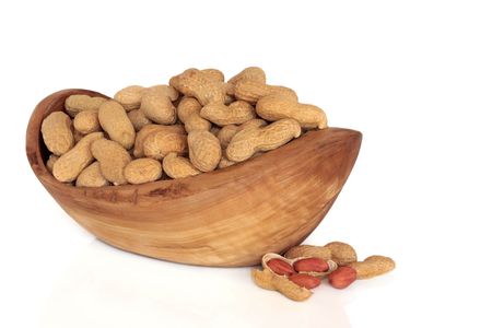 Peanuts in shells in an olive wood bowl and scattered, isolated over white background.の写真素材