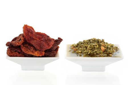Sun dried tomatoes and pesto sauce in white porcelain dishes  isolated over white background.の写真素材