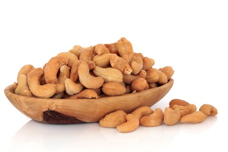 Cashew nuts in an olive wood bowl and scattered, isolated over white background with reflection.の写真素材