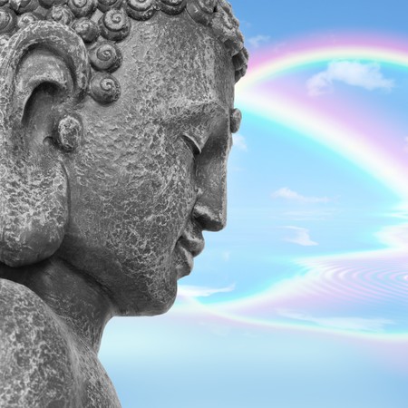 Face of a buddha with eyes closed in prayer, with a blue sky and double rainbow in reflection in the distance, symbolising nirvana.  Side view. の写真素材