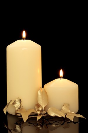 Christmas candles and golden ivy and holly berry leaf sprig over black background with reflection.の写真素材