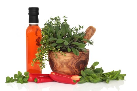  Chilli olive oil, chillies, and herb leaf sprigs of rosemary,  sage, thyme and oregano in an olive wood mortar with pestle, isolated over white background.の写真素材