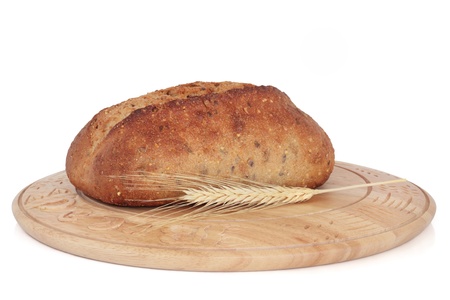  Wholegrain bread loaf on a rustic wooden bread board with wheat ear sprig, isolated over white background.の写真素材