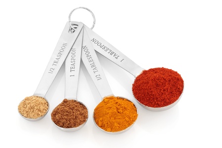 Spice selection of paprika, turmeric, chinese five spice and  ginger in stainless steel measuring spoons, over white background. Right to left.の写真素材