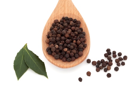 Black peppercorn spice in a wooden spoon and scattered with bay leaf herb, over white background.の写真素材