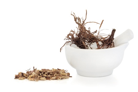 Valerian herb root in a porcelain mortar with pestle with a chopped pile to one side, isolated over white background. Valeriana. Modern day equivalent is valium and diazipam.