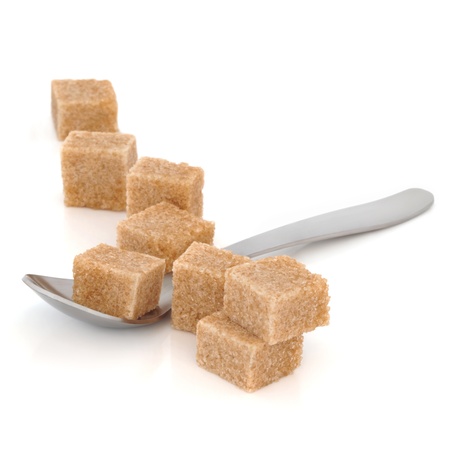 Brown sugar cubes in a spoon and scattered over white background. Selective focus.の写真素材