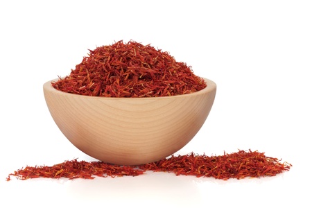 Saffron spice in a beech wood bowl and scattered, over white background. Used in chinese herbal medicine and for culinary purposes. Safflower. Hong hua. Flos carthami tinctori.の写真素材