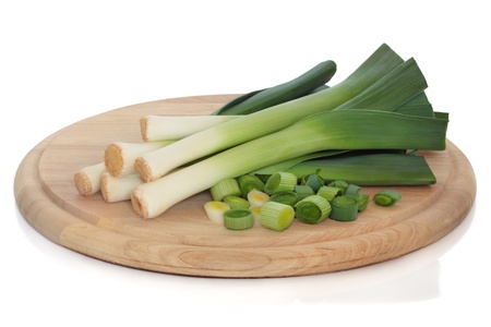 Leeks whole and chopped on a wooden bread board, isolated over white background.