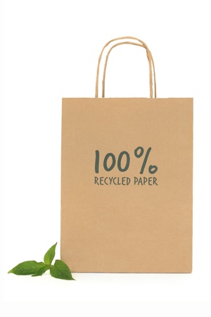 Recycled brown paper shopping bag with handle and green leaf sprigs, over white background.の写真素材