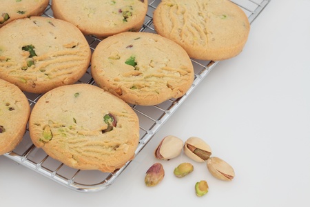 Pistachio shortbread biscuits on a cooling metal baking tray with scattered nuts to one side.の写真素材