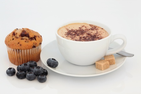 Cappuccino cup and saucer with chocolate chip muffin and loose blueberry fruit, over white background.の写真素材