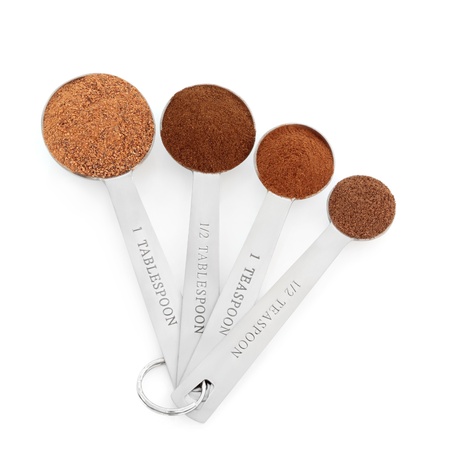 Spice selection of ground allspice, cinnamon, clove and nutmeg in stainless steel measuring spoons isolated over white background.の写真素材