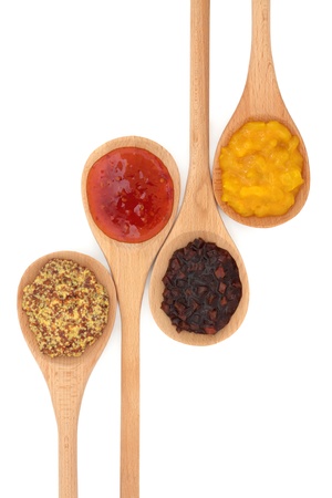 Wholegrain mustard, chili sauce, sweet vegetable pickle and piccalilli, in wooden spoons isolated over white background.の写真素材