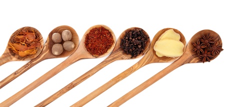 Cloves, ginger, saffron, nutmeg, star anise and mace spice in olive wood spoons over white...
