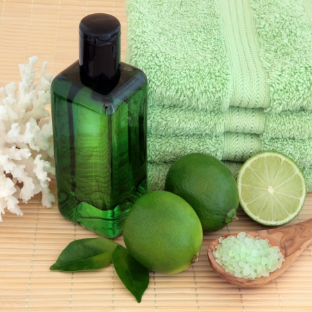 Lime fruit with spa accessories of green towels, bubble bath, sea salt and coral shell over bamboo background の写真素材