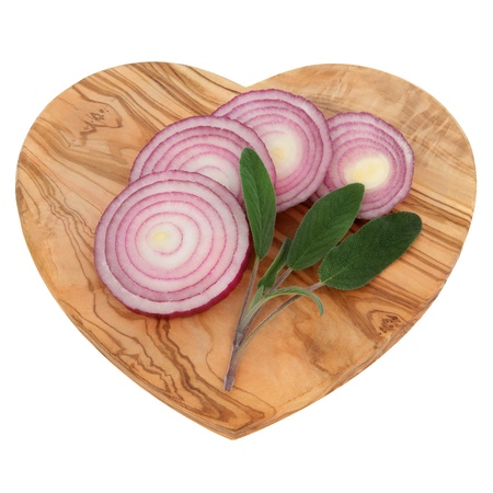 Sage herb leaf sprigs and red onions sliced on an olive wood heart shaped board over white background の写真素材