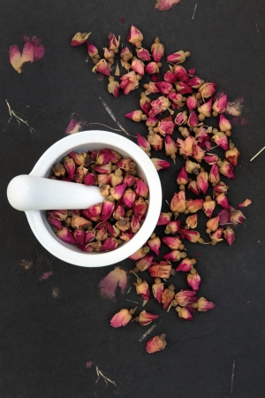 Rosebud flower heads in a white mortar with pestle over rose impregnated black paper, used in chinese herbal medicine の写真素材