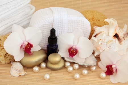 Orchid flower still life with gold spa stones, aromatherapy oil bottle, sea shells and pearls with sponge and towels over bamboo の写真素材