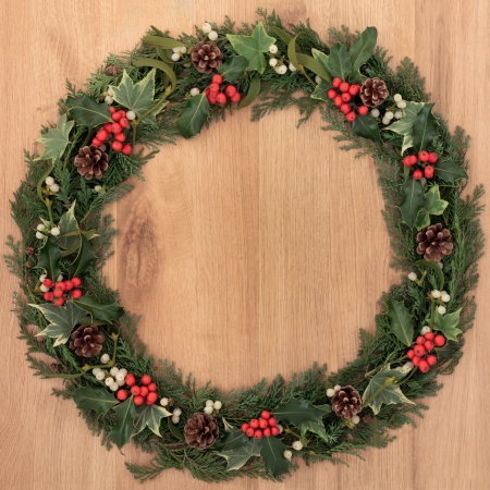 Christmas wreath with holly, mistletoe, ivy, pinecones and cedar leaf sprigs over golden oak background の写真素材