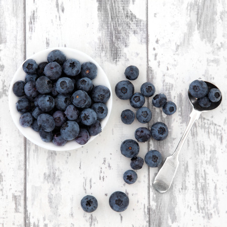 Blueberry fruit in a white bowl and silver spoon over distressed wooden background 