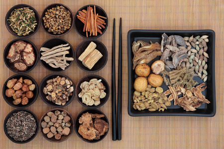 Large chinese herbal medicine selection in wooden bowls and square dish with chopsticks over bamboo の写真素材
