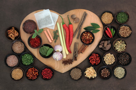 Herb and spice selection on a heart shaped board in wooden bowls and loose の写真素材
