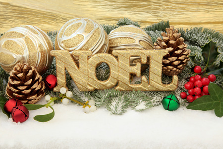 Christmas noel sign with gold bauble decorations, holly and winter greenery over snow background の写真素材