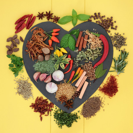 Herb and spice ingredients on a heart shaped slate and loose over yellow wooden background.の写真素材