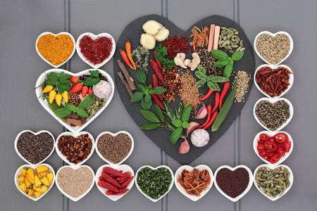 Herb and spice ingredients on a heart shaped slate and in porcelain dishes over wooden grey background.の写真素材