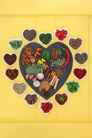 Herb and spice ingredients on a heart shaped slate and in porcelain dishes over yellow wooden background.の写真素材