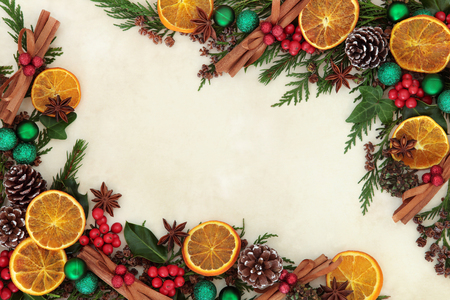 Christmas background border with dried fruit and spices, green bauble decorations, holly and winter greenery over old parchment paper. Christmas background border with dried fruit and spices, green bauble decorations, holly and winter greenery over old parchment paper.