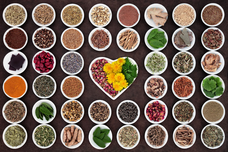 Herbal medicine selection used for womans health in heart and round shaped porcelain bowls over lokta paper background.