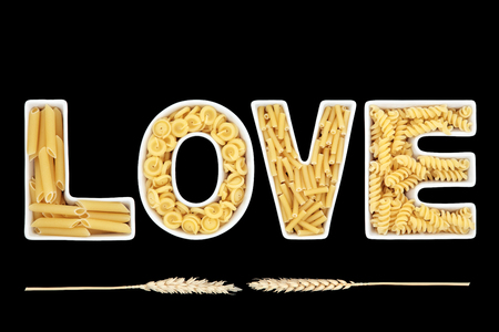 Love word of white porcelain china letters with pasta types with ears of wheat over black background.の写真素材